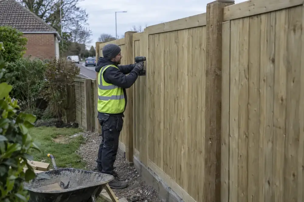 Fence installation worker fixing a substantial timber acoustic barrier alongside a garden